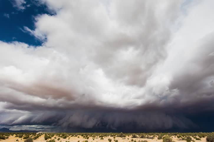 A blue sky with white clouds quickly darkens as storm clouds gather and surge over a desert