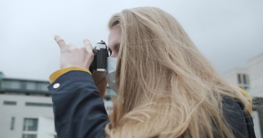 Female wearing a medical mask taking a photograph in downtown area