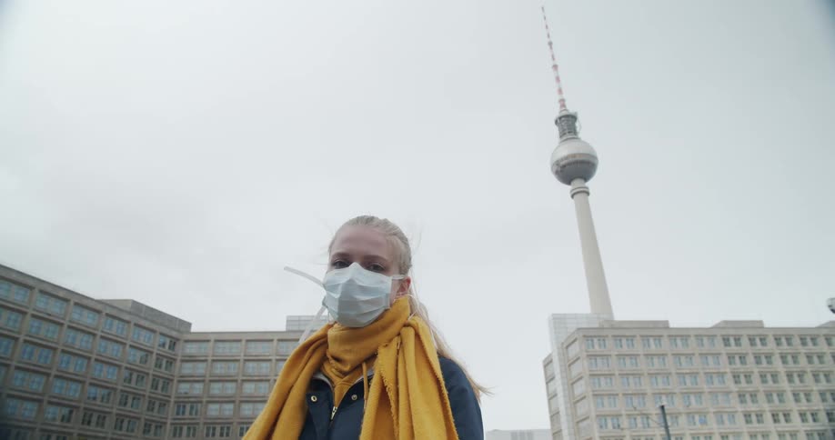 Woman wearing face mask stands in front of the berlin television tower