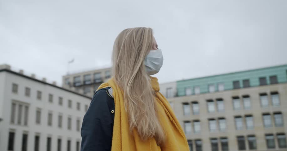 Blonde woman wearing a face mask due to corona virus stands in front of the brandenburg gate a historical place in berlin