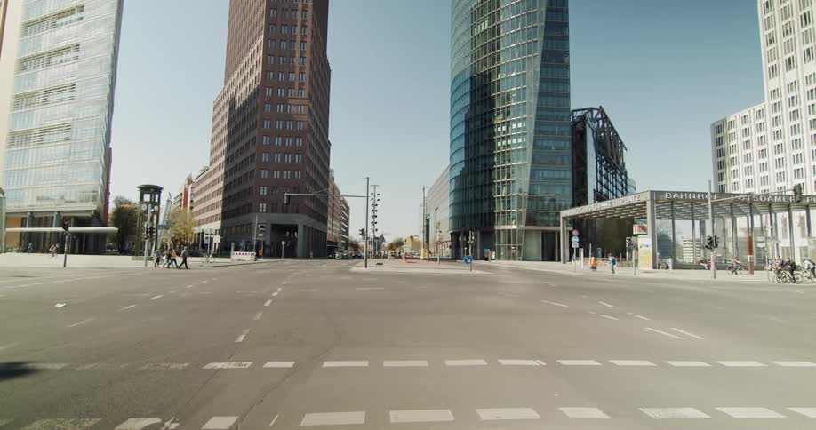 People cross a large empty city street by bicycle or walking as cars wait at the traffic light