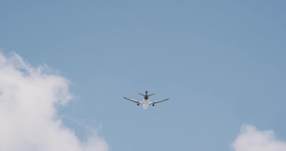 An airplane flying overhead in a bright blue sky with white clouds