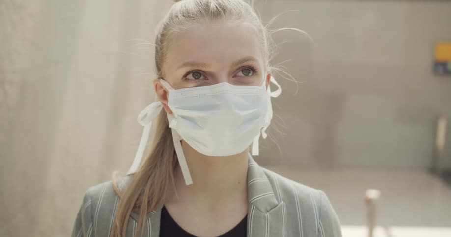 A young woman wearing a medical masks walks while looking into the air