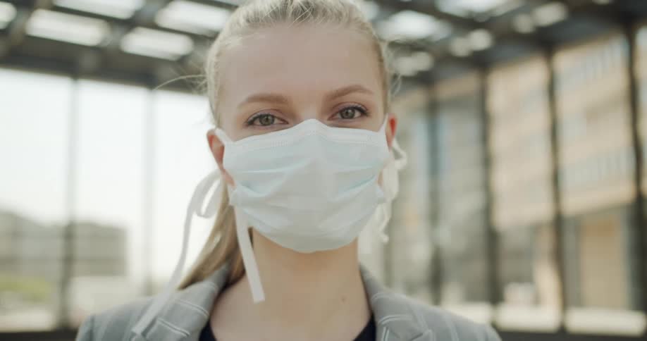 A woman in a medical face mask looking into the camera while standing outdoors during the day