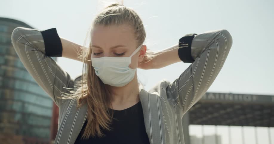Blonde woman wears a white face mask outdoors as a precaution due to coronavirus
