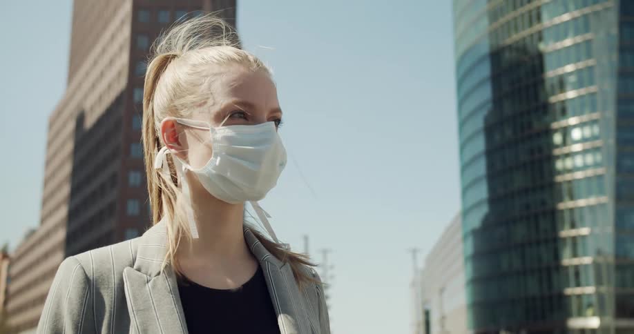 A woman wearing a mask stands in a downtown area