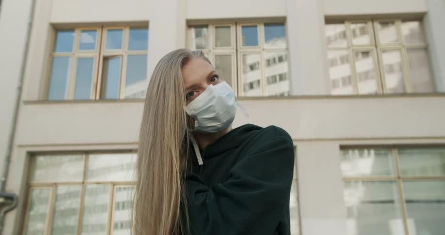 A woman adjusts her face mask by the building