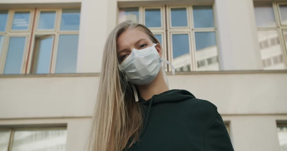 A woman wearing a surgical mask poses in front of a building