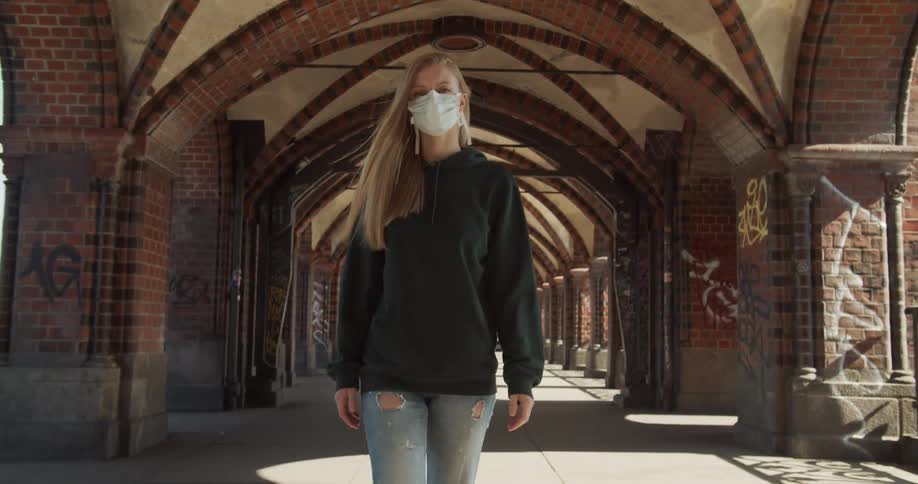 Woman wearing a white face mask due to coronavirus walks in the building