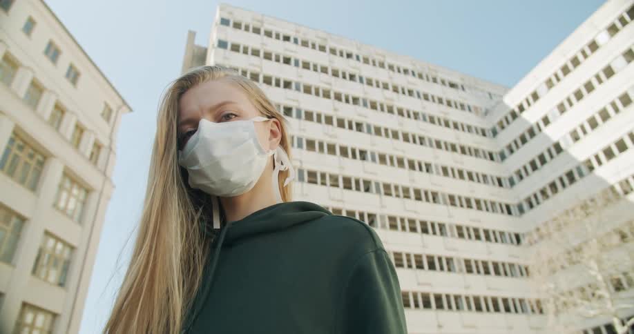 A woman standing with a mask on with buildings in the background