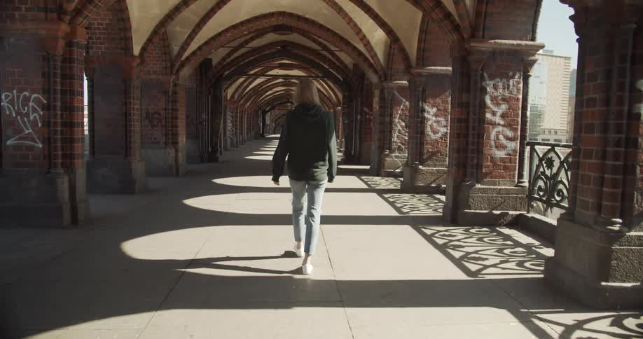 Woman walks past columns decorated with graffiti under an arched roof