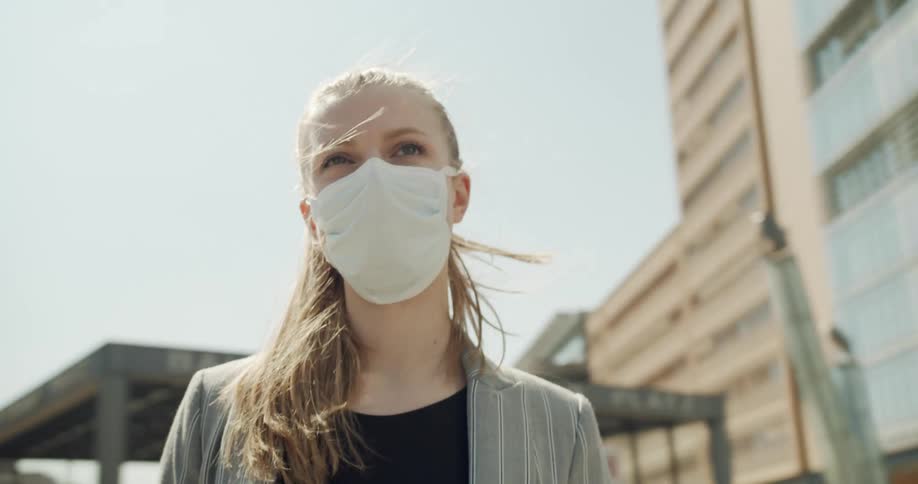 A woman standing on the street with a mask on with buildings surrounding her