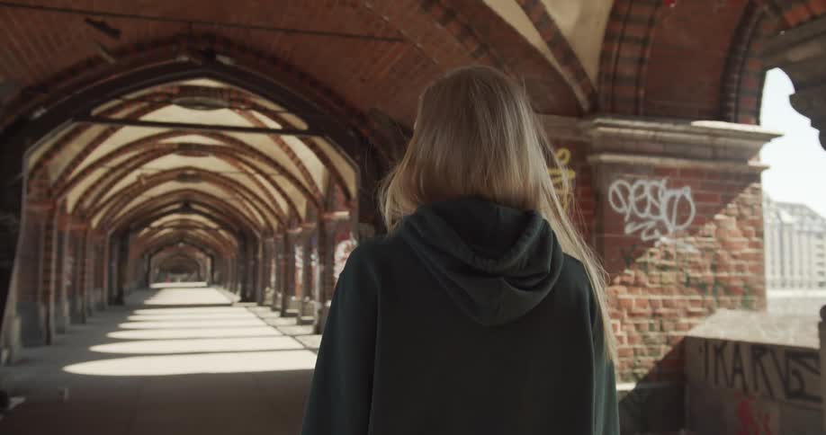A woman walks down a long exterior corridor of a large building