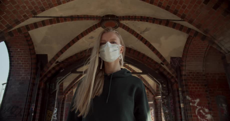 A woman standing underneath an arch hallway with a mask on