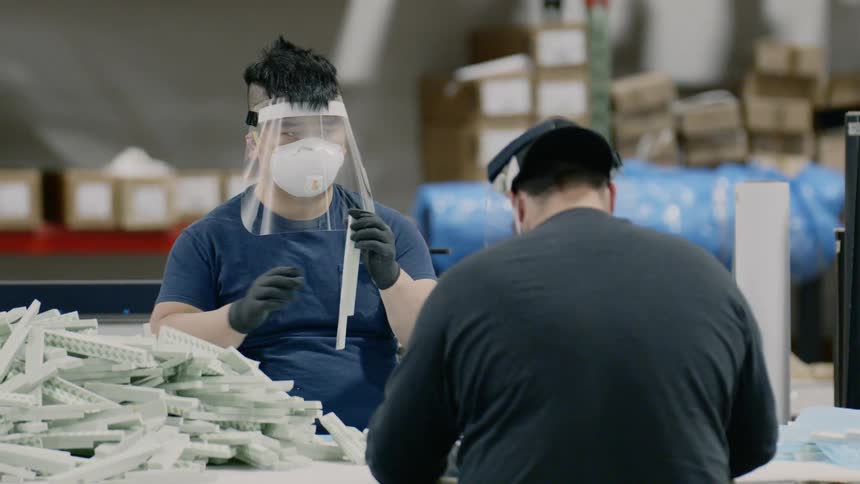 Workers wearing face masks assemble products in warehouse
