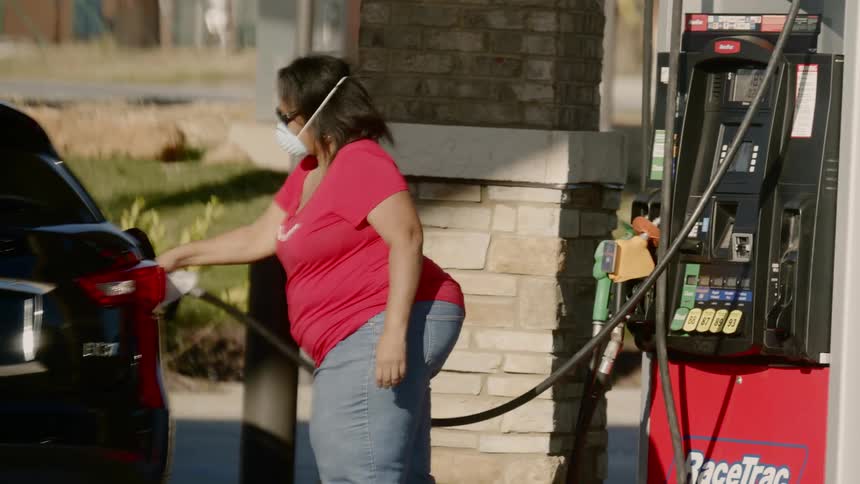 Woman wearing face mask fills a cars tank in gas station at day