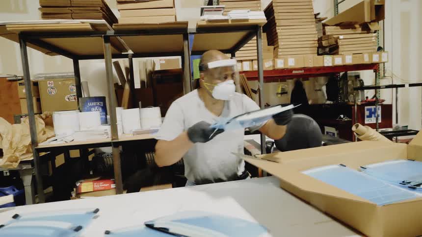 A man packs plastic face masks into a box for shipping
