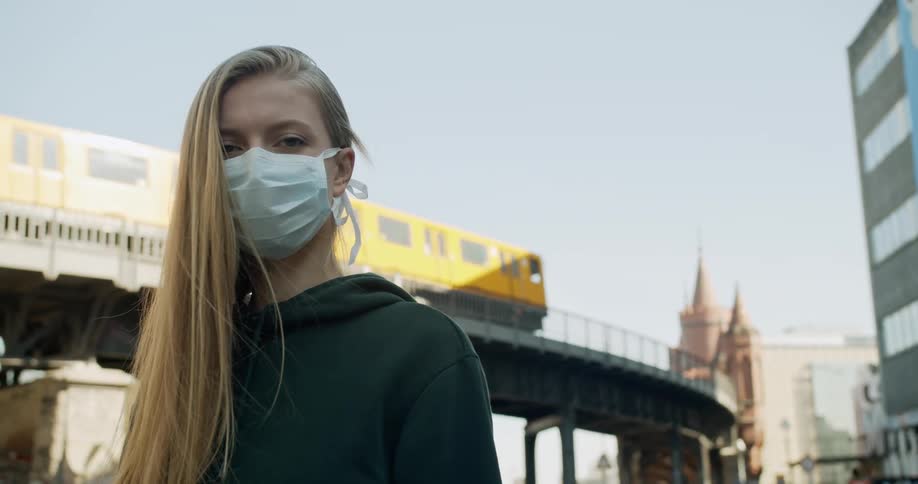 A woman stands by a train platform wearing a face mask
