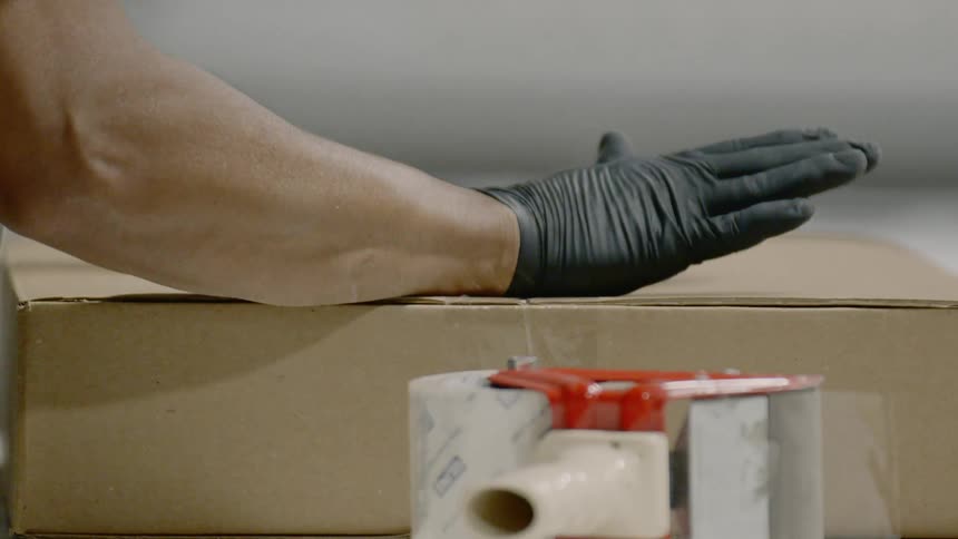 Person wearing gloves seals cardboard box with tape