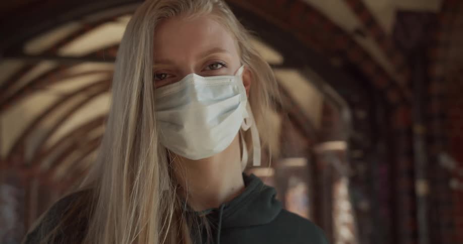 Woman wearing mask and hoodie stands under arched roof