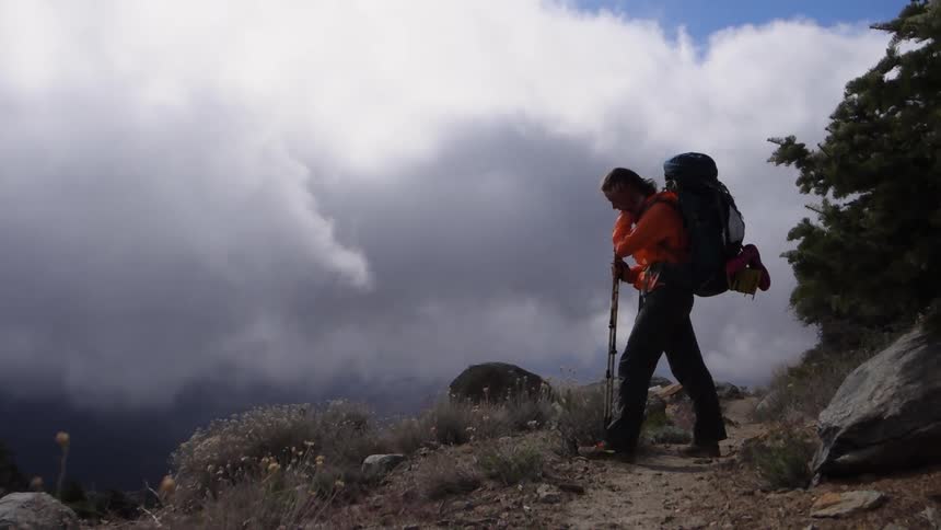 A hiker overlooks the edge of a mountain as clouds roll in