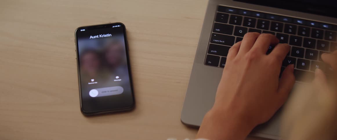 Woman working on laptop picks up smartphone to take a call