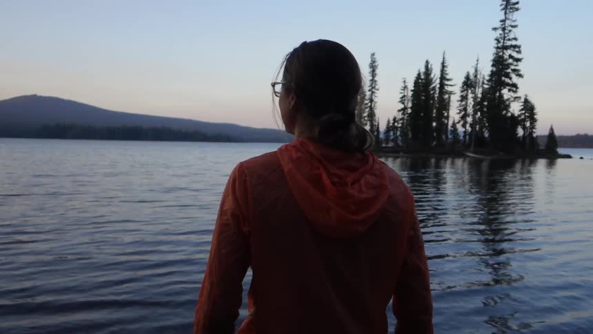 A woman is walking waist high into a lake at sunset
