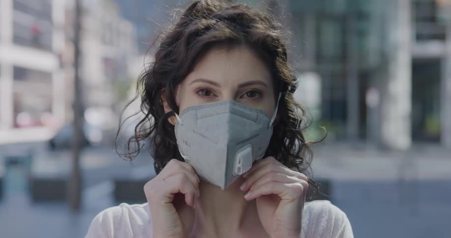 A woman puts on a protective mask while standing on a city street