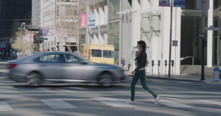A woman in a face mask walking across the street at a crosswalk in a city