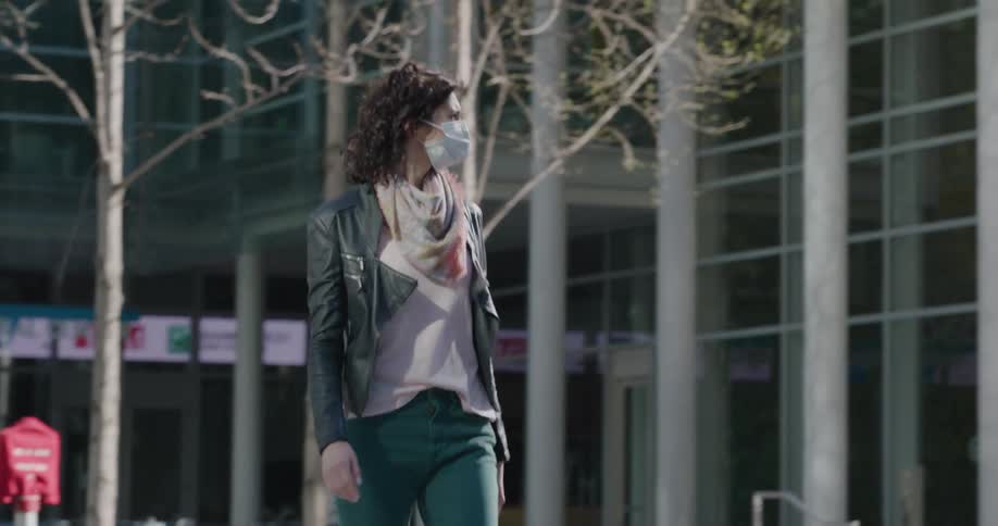 Woman wearing a white face mask as a precaution due to corona virus walks in the city square