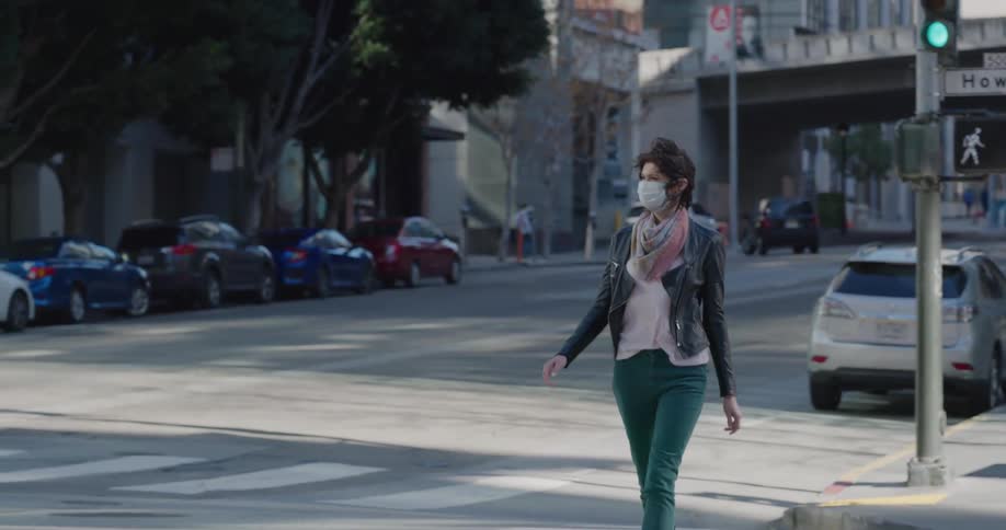 A woman wearing a face mask walks down a city sidewalk as traffic passes by