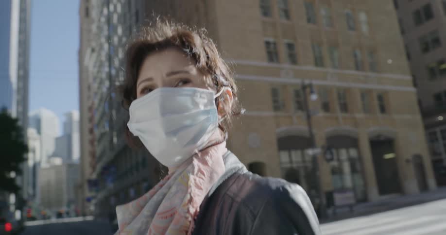 A woman wearing a mask looks around as she walks through a nearly empty city