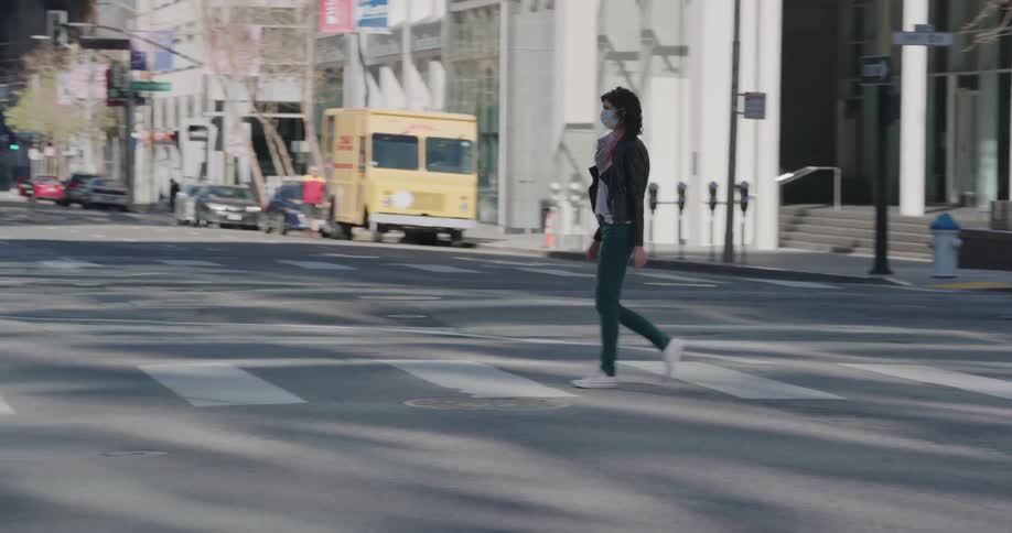 A woman walking across the street in a face mask
