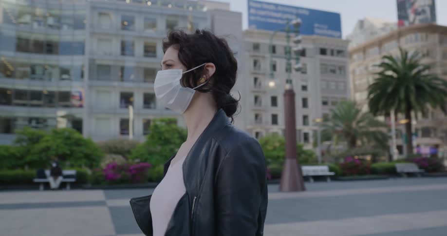 A woman walking outside surrounded by buildings with a mask on