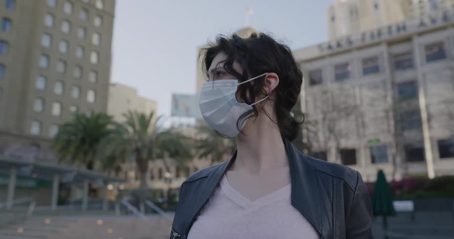 A woman wears a mask and looks around a city
