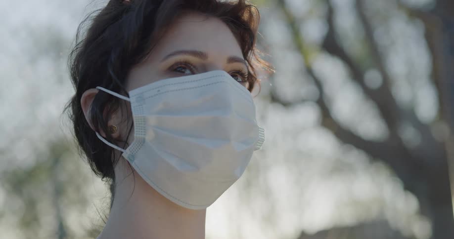 A woman looks around outdoors while wearing a mask