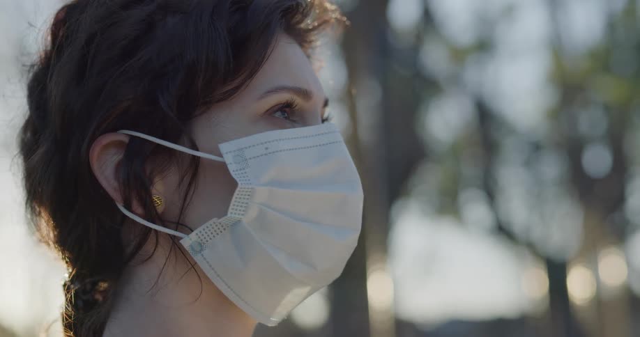 A woman looks around outdoors while wearing a mask