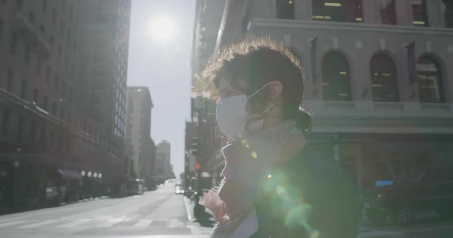 A woman wears a face mask while standing in a city intersection