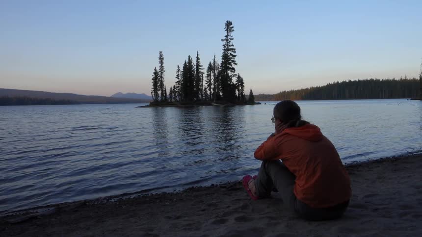 A woman sits on the beach of a rippling lake