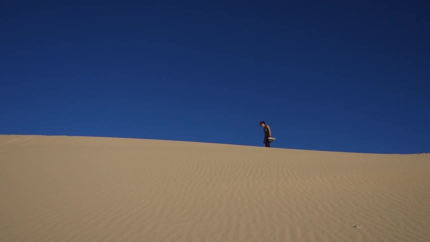 A person walks across a sand dune in the daytime