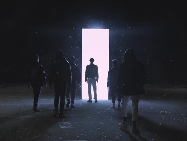 Men stand and walk across parking lot toward glowing white rectangle