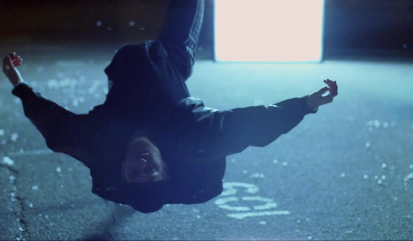 Man floats unmoving in midair at night near white rectangle of light