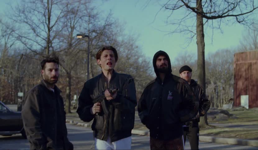 A man walks through a small crowd holding an automatic rifle and starts shooting
