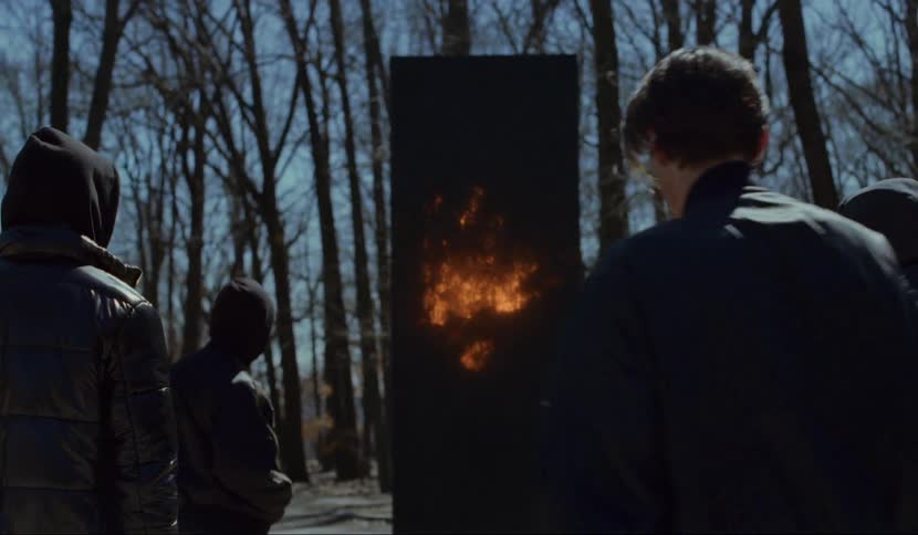 A man approaches a large black panel that is glowing and transmitting passing a group that are captivated and staring at the box