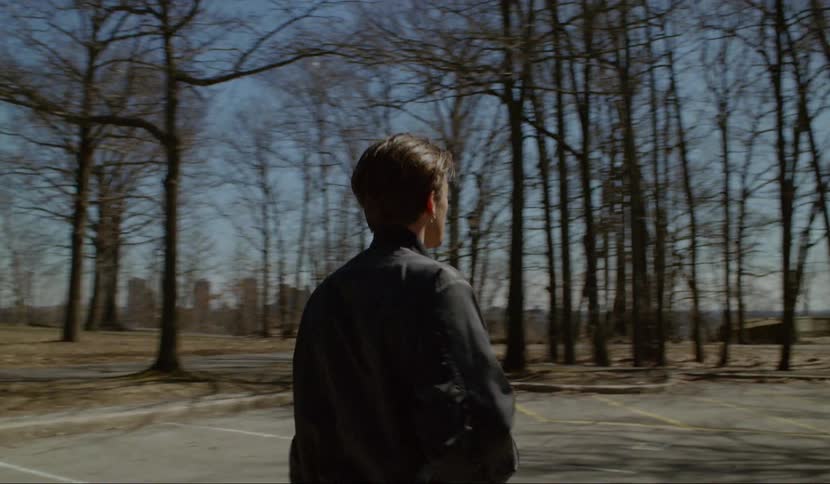A man walking through a group of men to approach a glowing black monolith in a parking lot