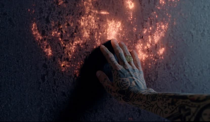 A tattooed hand touches a glowing wall