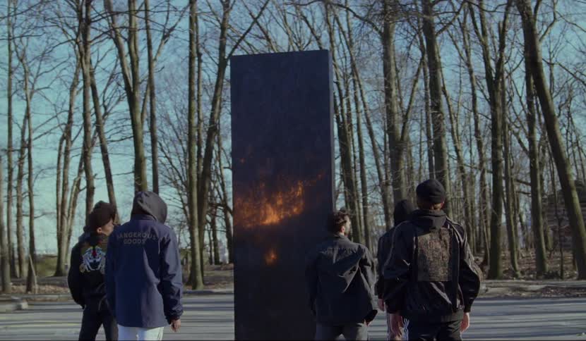 Six men standing in front of a black pillar that is glowing orange