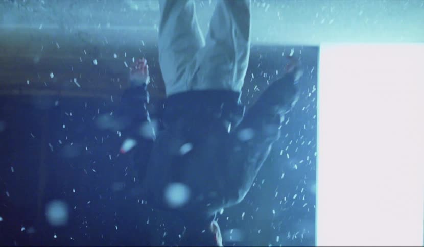 An upside down look at a man standing outside at night in front of a large glowing light while white flakes float around him