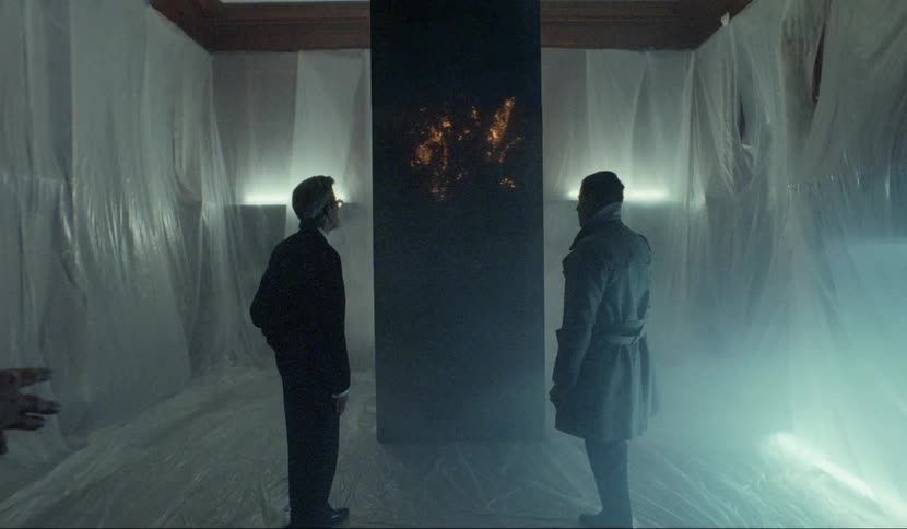 Men stand in plastic sheet shrouded room examining dark obelisk glowing from within