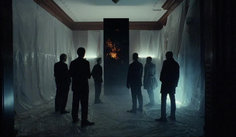 A group of men standing before a glowing black monolith in a room covered in plastic